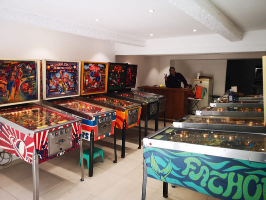 Row of Bally and Gottlieb pinball machines standing on their chrome legs in a game room
